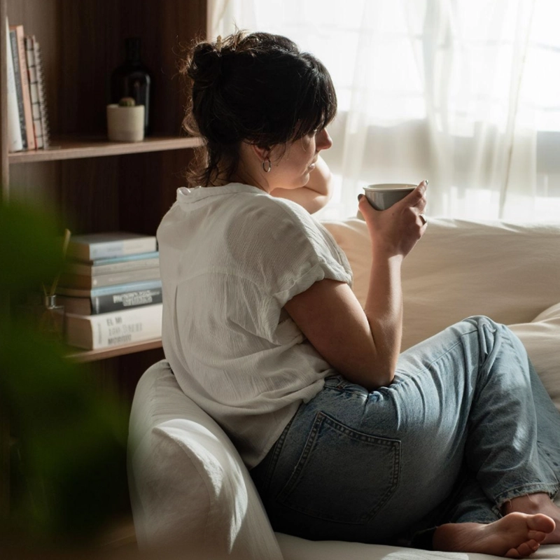 Fabiana, fundadora de Mutatis Estudio, de perfil junto a una ventana con una taza en la mano, en actitud reflexiva